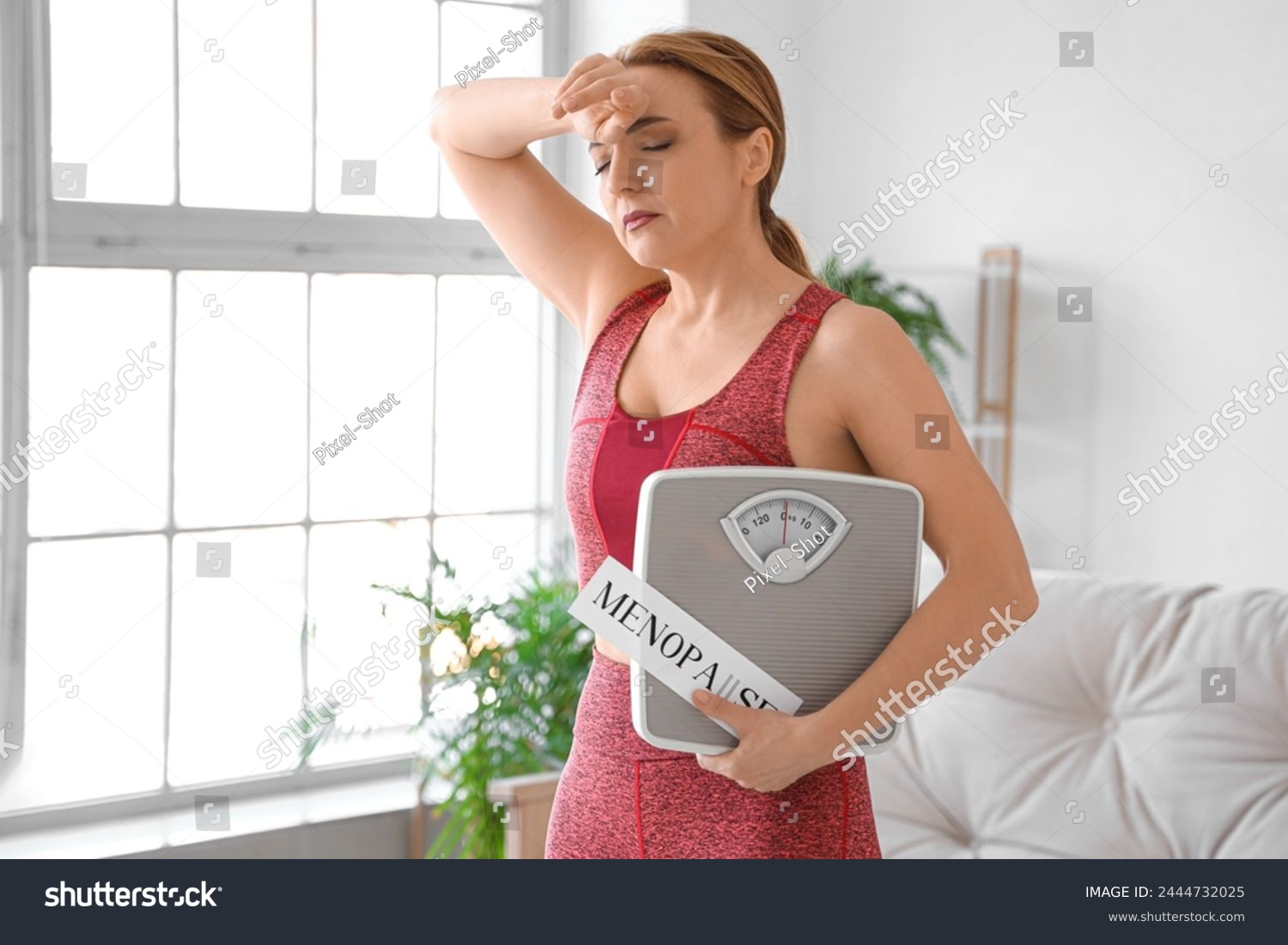 stock-photo-sporty-mature-woman-holding-paper-with-word-menopause-and-weight-scales-at-home-2444732025
